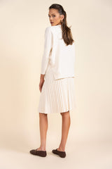 Woman wearing a white blazer and pleated skirt on a beige background