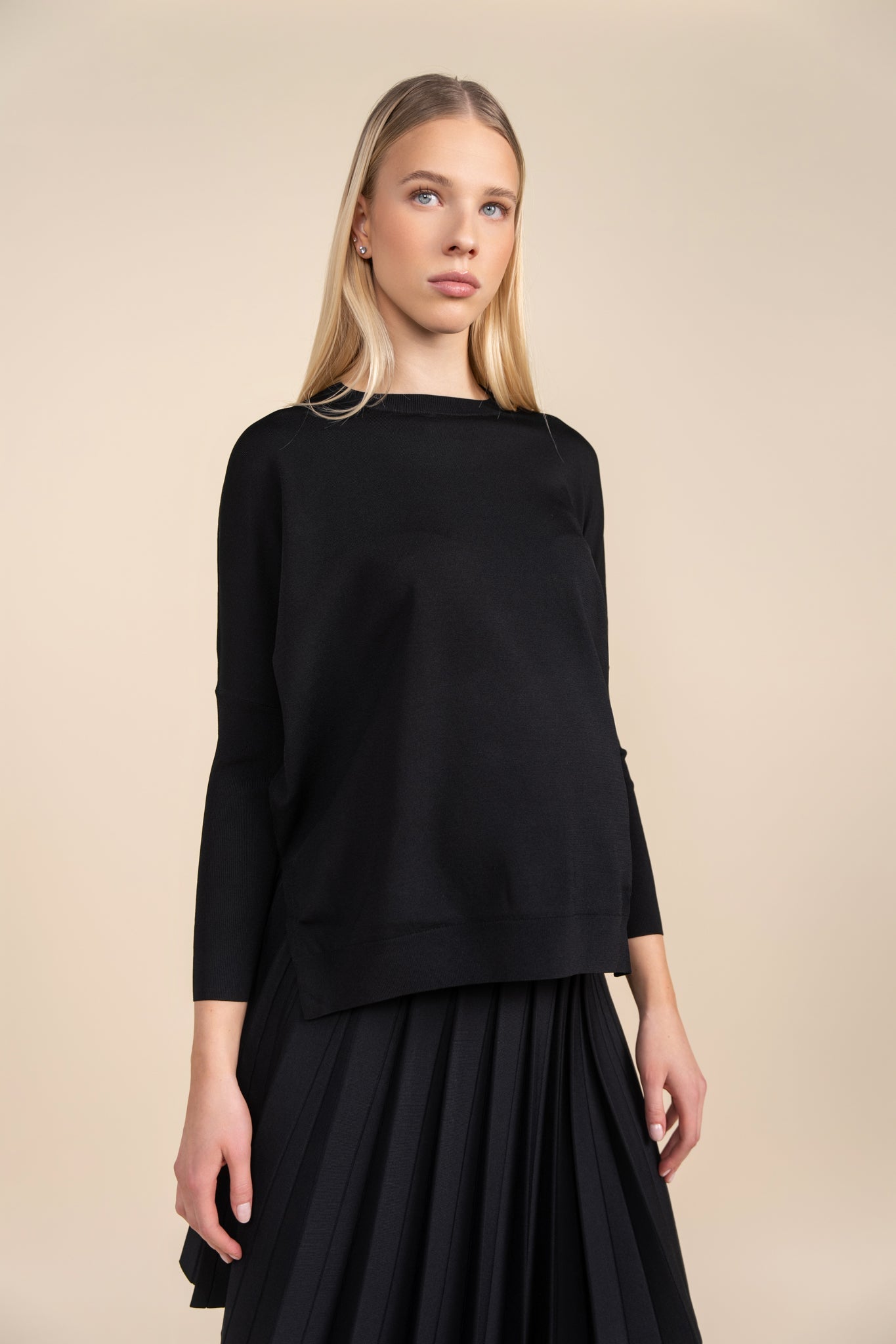 Woman wearing a black top and black skirt against a beige background