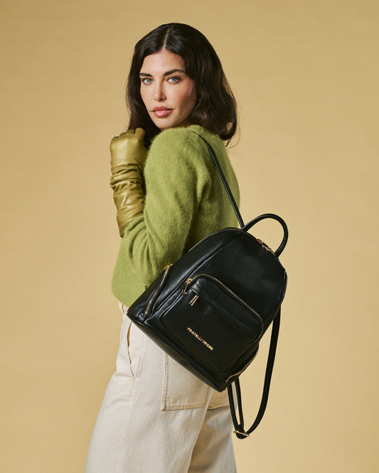 Woman wearing a green sweater and beige pants with a black backpack on a beige background