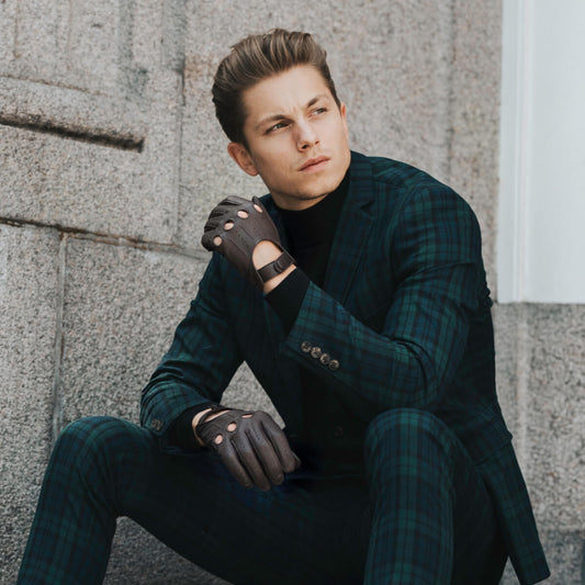 Man in a dark green plaid suit sitting against a stone wall.