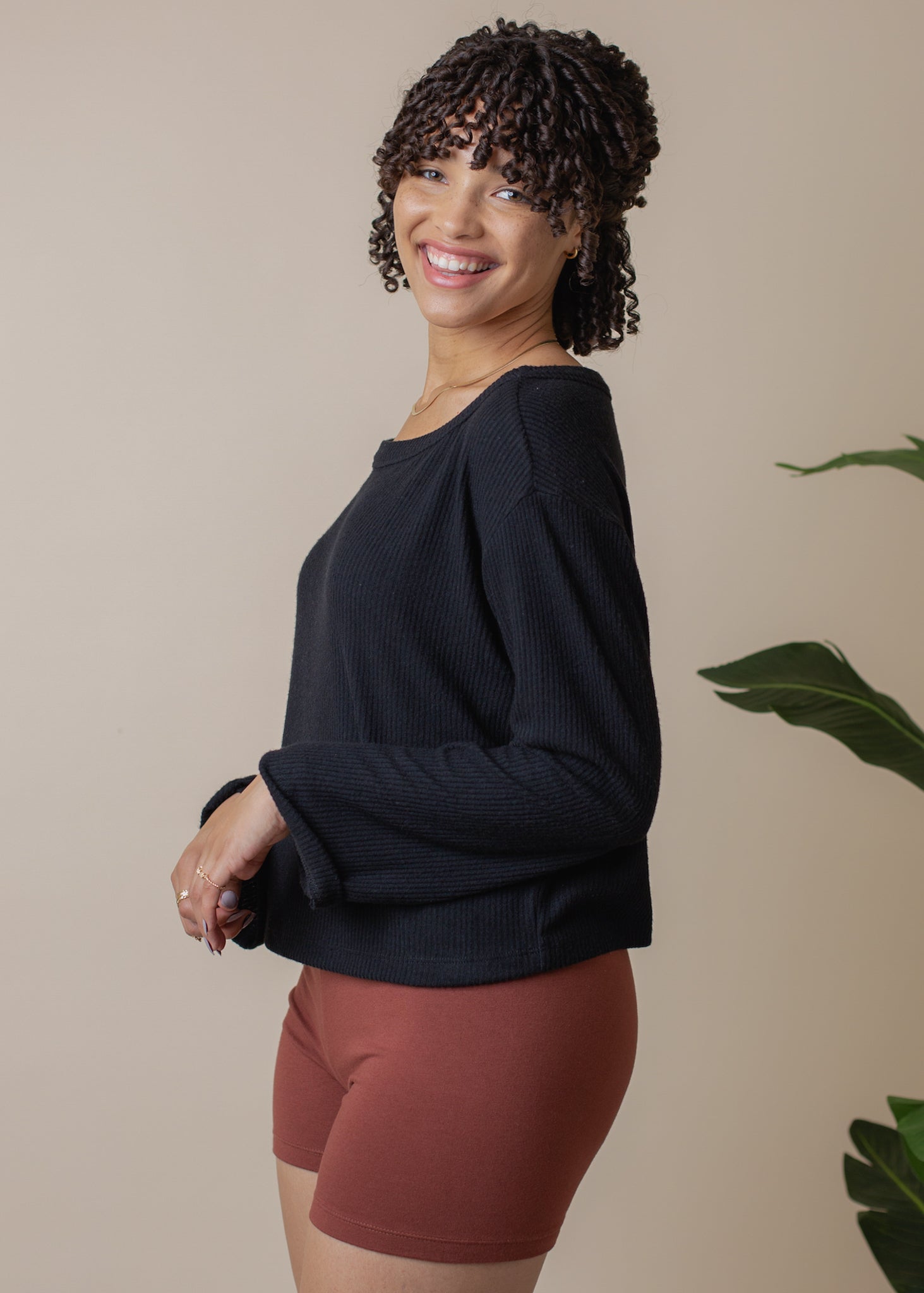 Woman wearing a black long-sleeve top and maroon shorts against a beige background