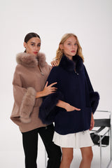 Two women wearing fur-trimmed ponchos against a white background