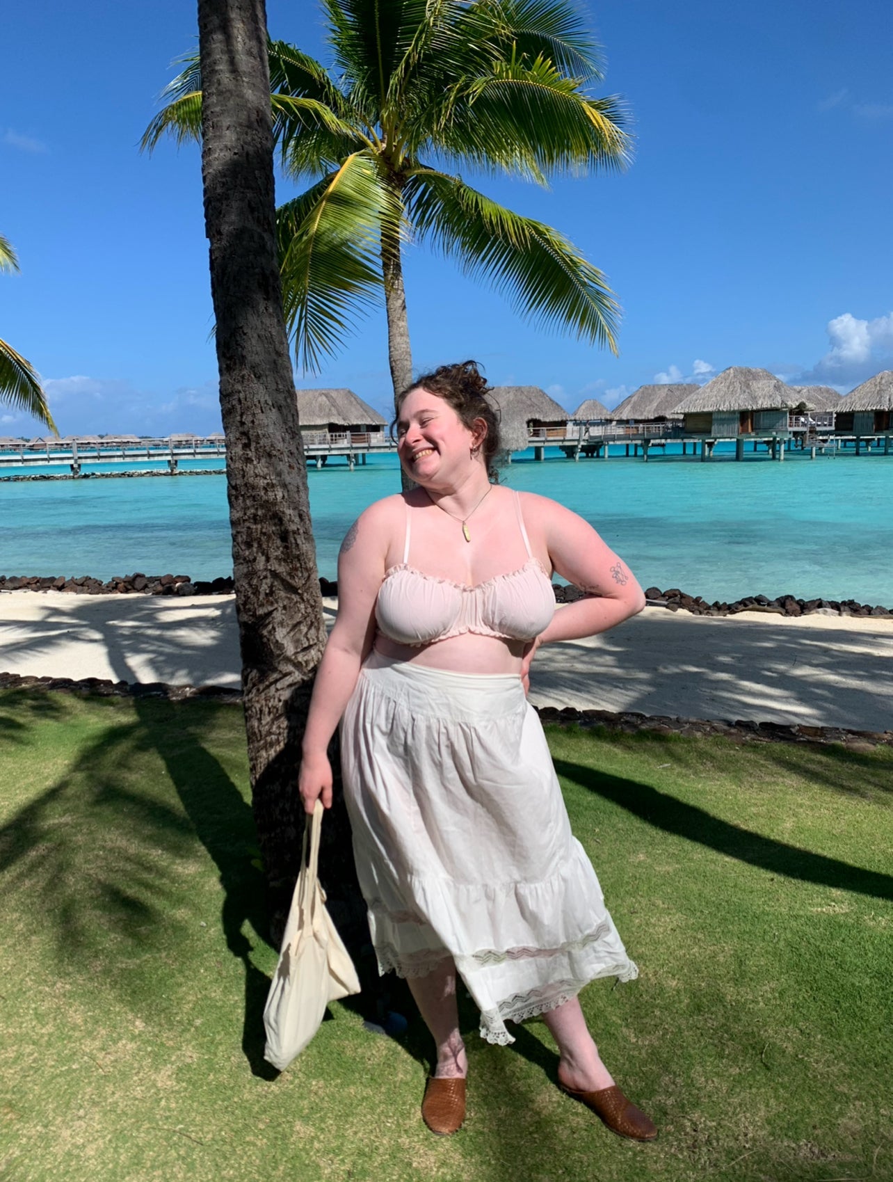 Woman standing on a grassy area with palm trees and a clear blue sky in the background.