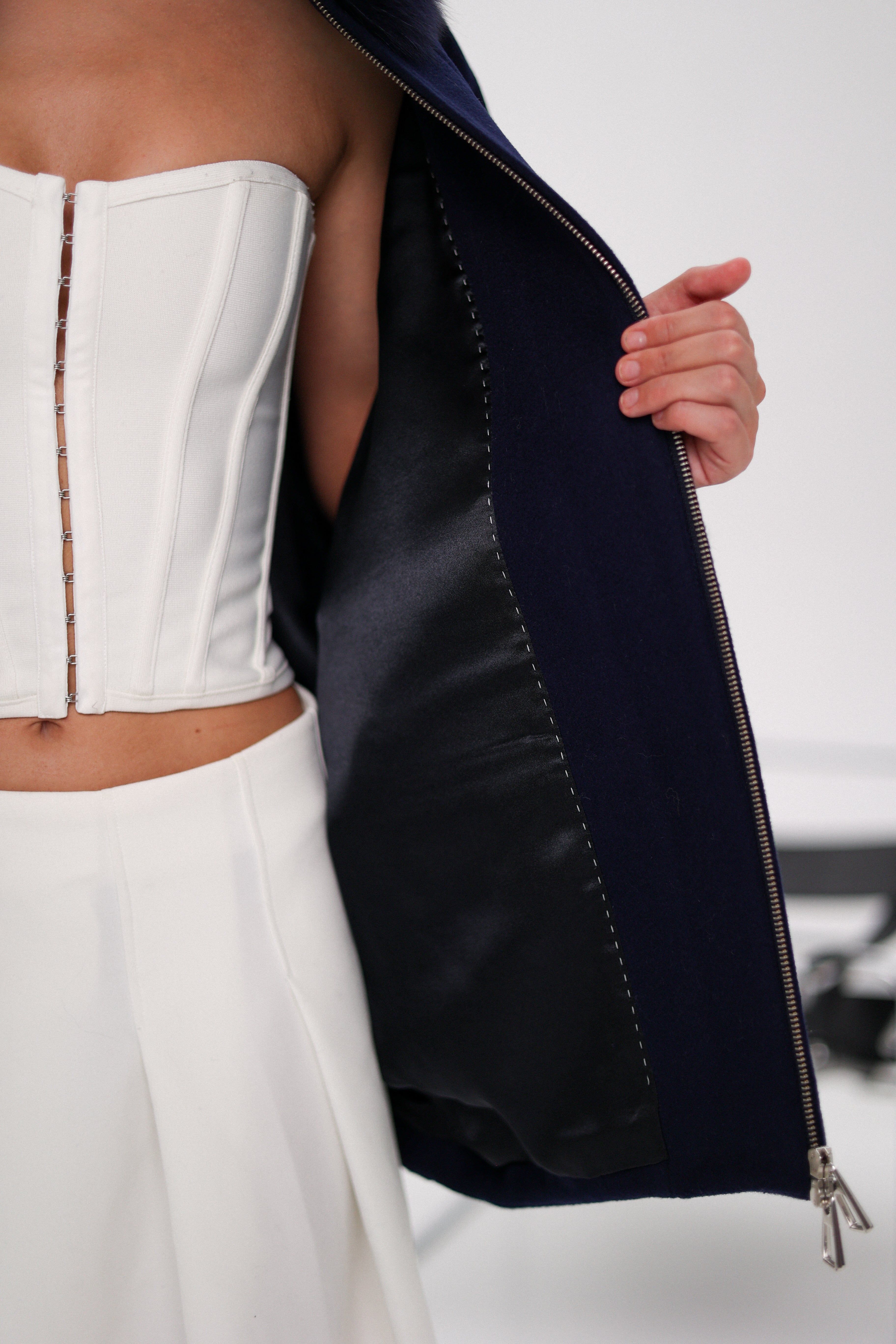 Person wearing a white strapless top and pants with a navy jacket, on a plain background