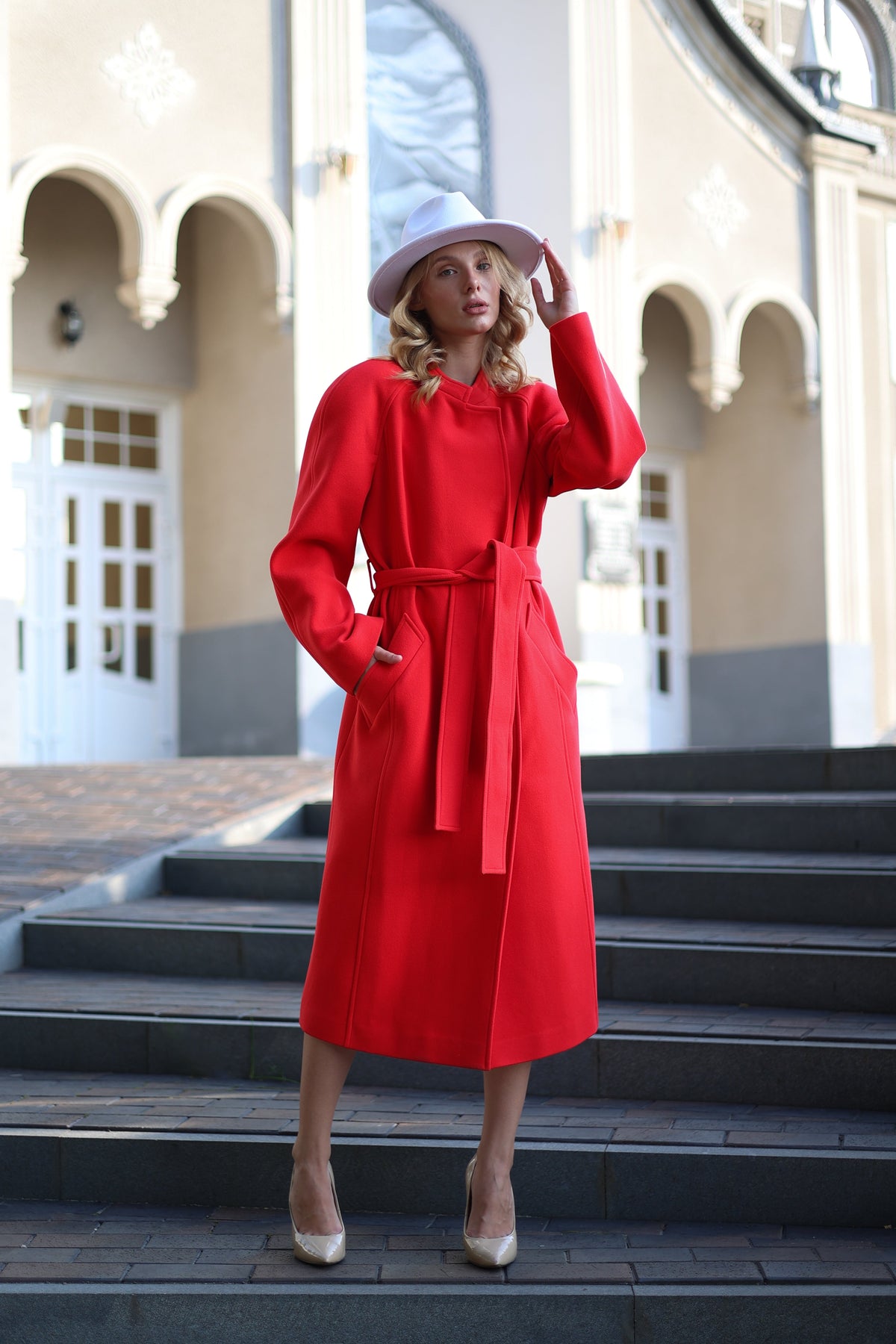 Woman in a red coat and white hat standing on steps outdoors