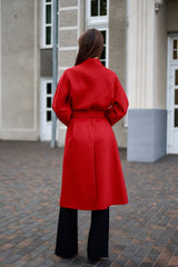 Person wearing a red coat standing on a paved area with a building in the background