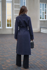 Woman wearing a long dark coat standing on a paved area with a building in the background