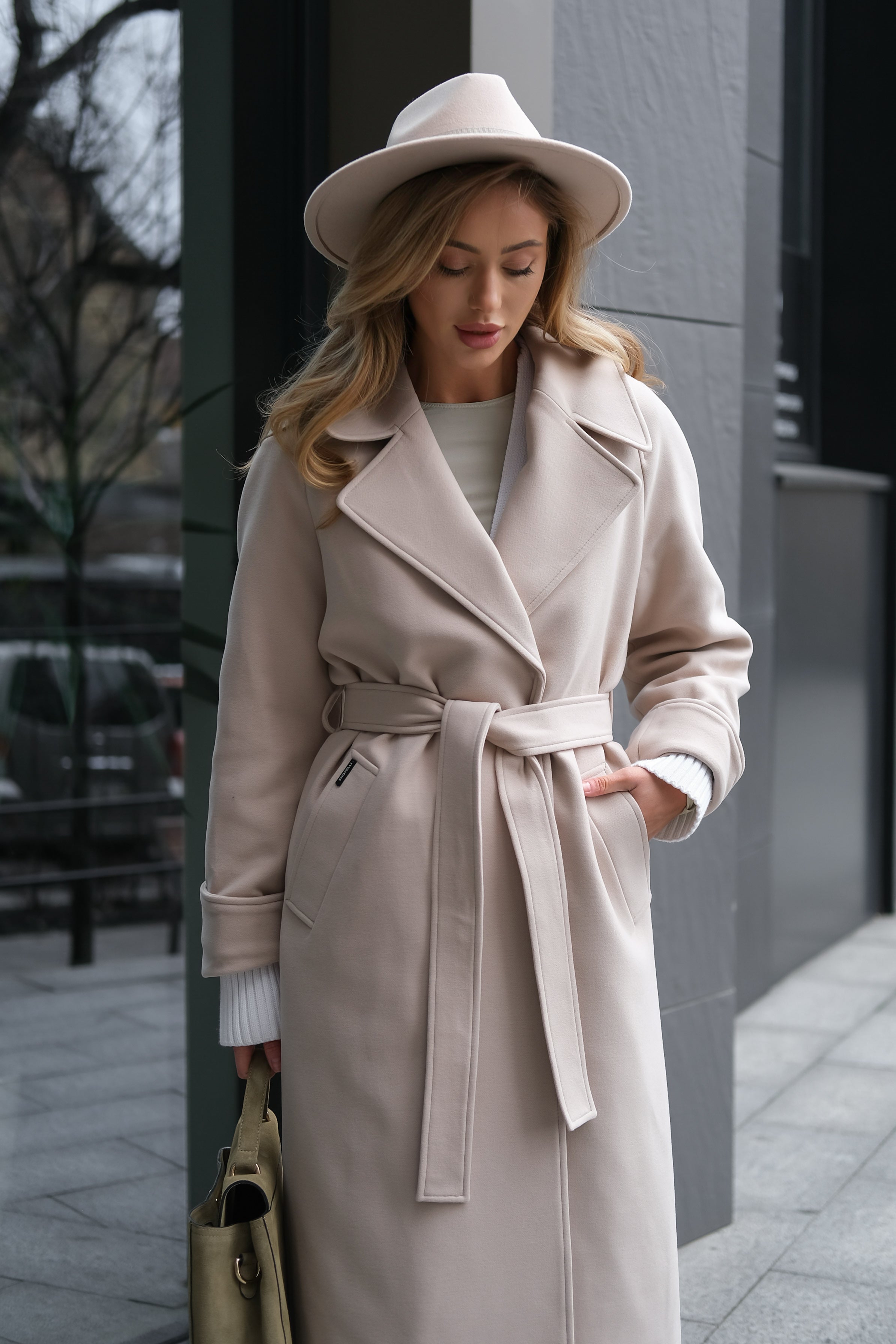 Woman wearing a beige trench coat and hat on a city street.