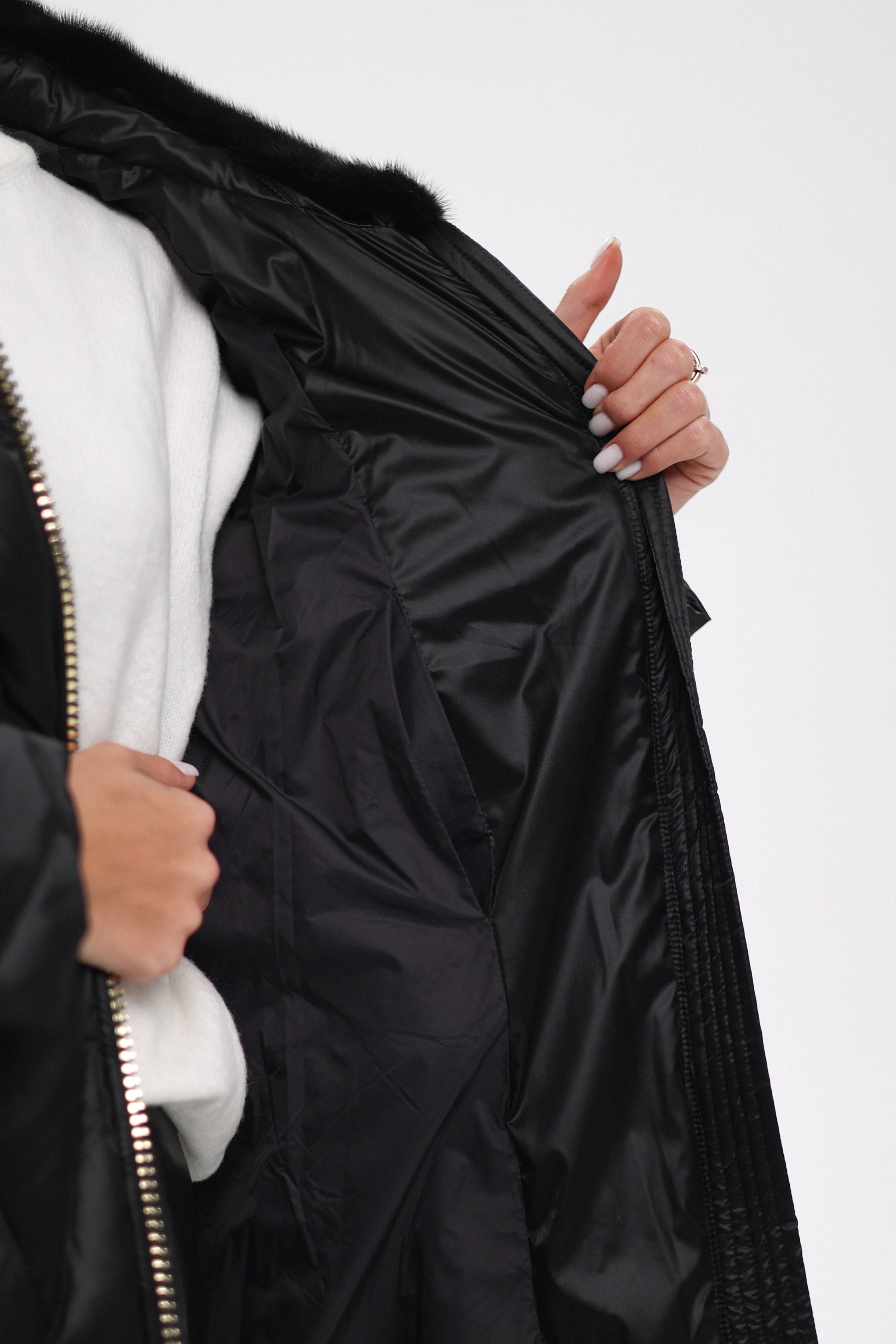 Close-up of a person holding a black puffer jacket with a white interior on a light gray background