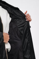 Close-up of a person holding a black puffer jacket with a white interior on a light gray background