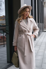 Woman wearing a long beige coat and hat on a city street.