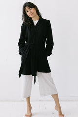 Woman wearing a black coat and white pants against a white background