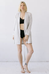 Woman wearing a black lace top and black shorts with a beige robe over her shoulders against a white background.