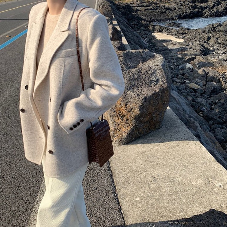 Person wearing a beige coat and holding a brown bag on a rocky coastal path.