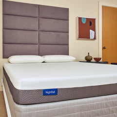 Mattress with 'Nightfall' label on a bed in a room with a headboard and wall art.