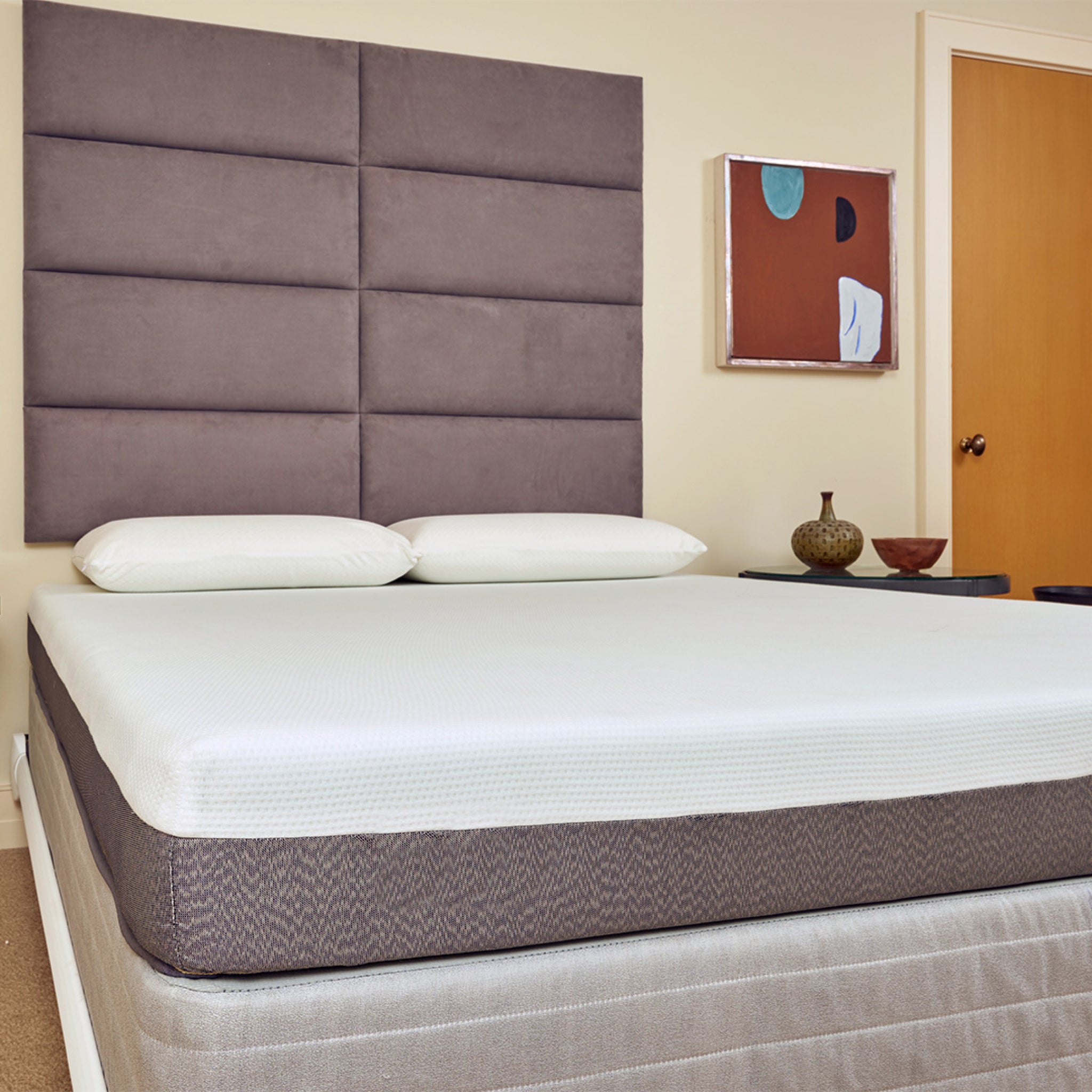 Bed with gray mattress and headboard in a room with a door and wall art.