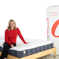 Woman in red sweater sitting on a mattress with a large Quidi Vidi box in the background.