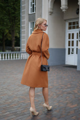 Woman in a brown coat walking on a brick pavement with a building in the background