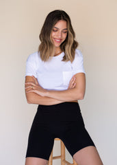 Woman wearing a white t-shirt and black shorts against a beige background