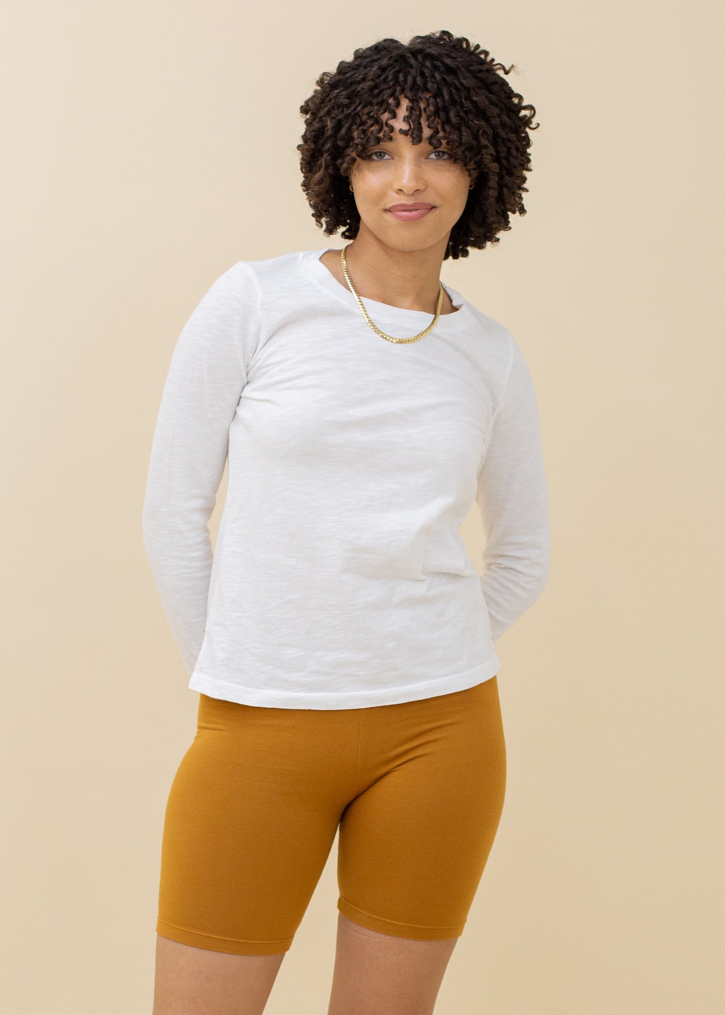 Woman wearing a white long-sleeve shirt and mustard yellow shorts on a beige background