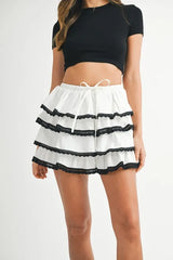Woman wearing a black crop top and white skirt with black lace trim on a white background