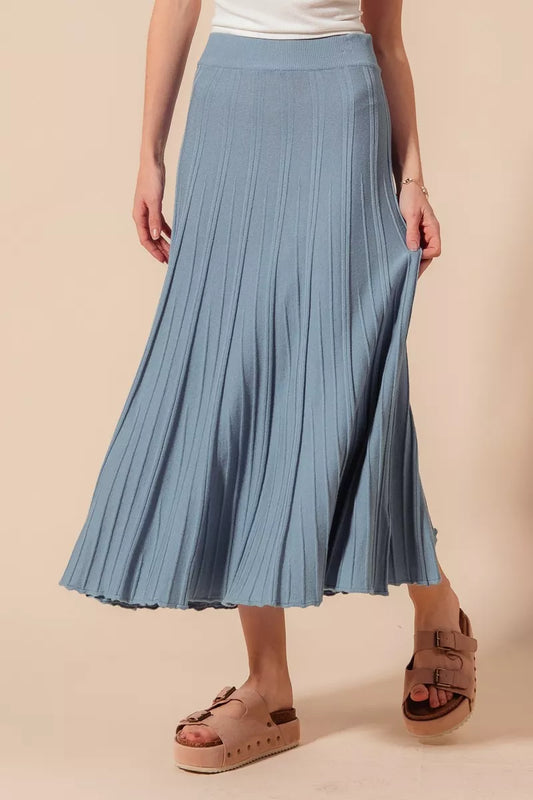 Person wearing a blue pleated skirt on a beige background