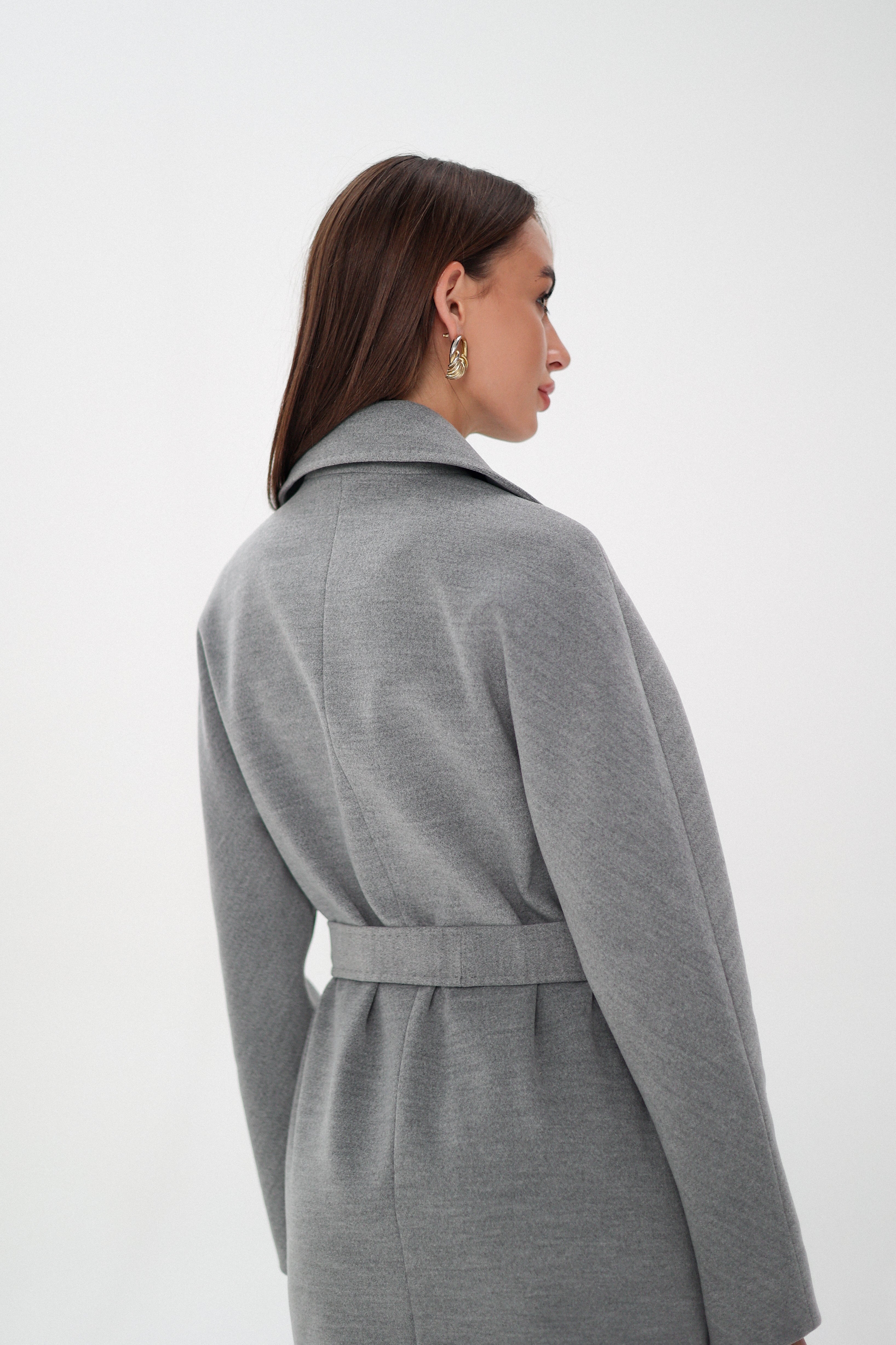 Woman wearing a gray coat over a black outfit on a white background