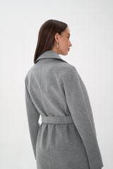 Woman wearing a gray coat over a black outfit on a white background