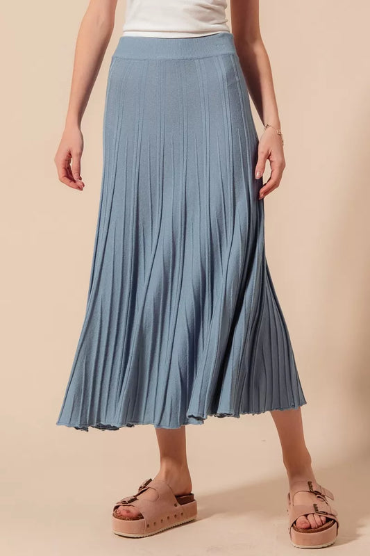Person wearing a blue pleated skirt on a beige background