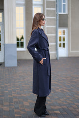 Woman wearing a long navy coat standing on a paved walkway.
