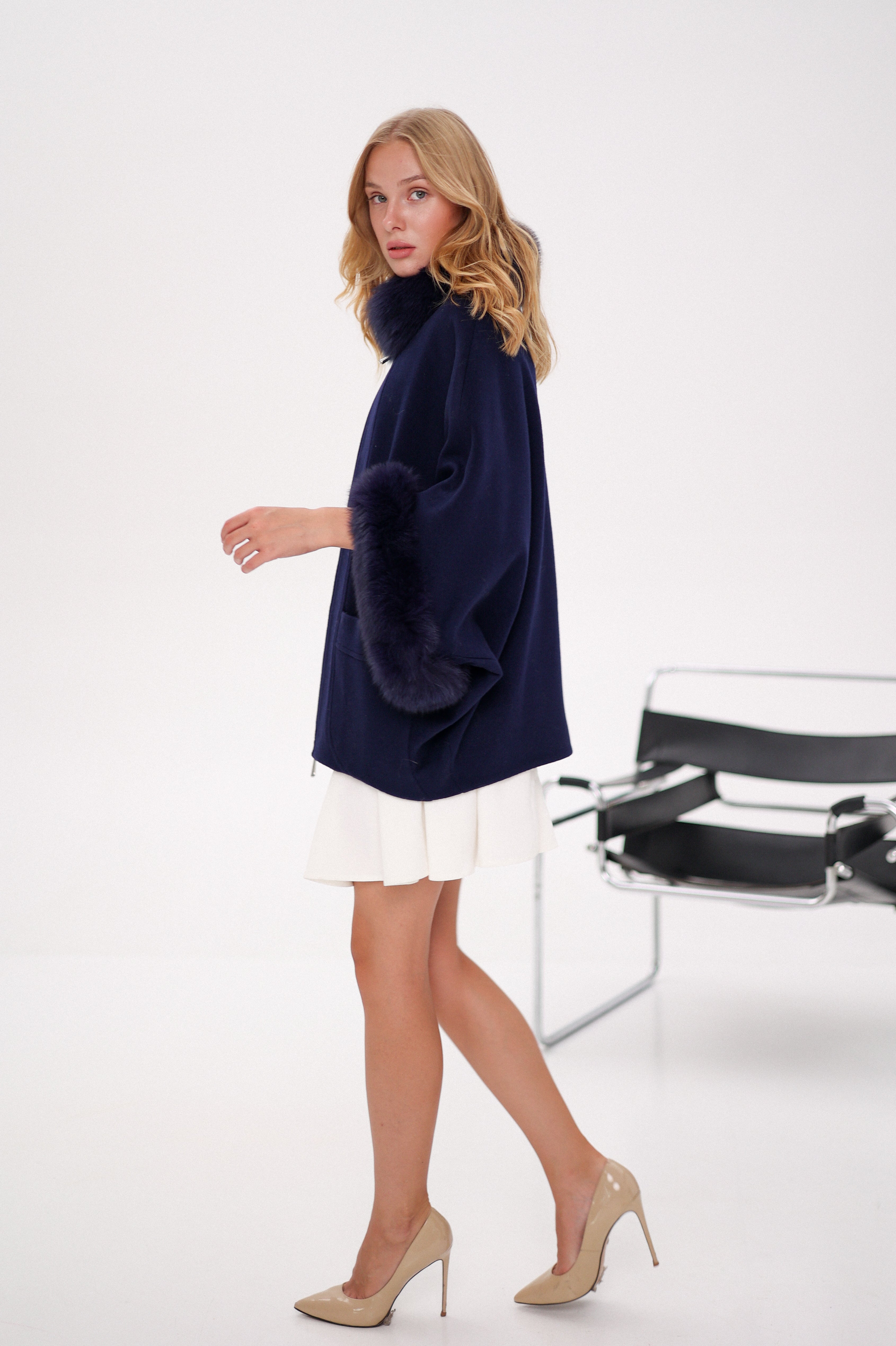 Woman wearing a navy blue poncho over a white dress with beige high heels on a white background
