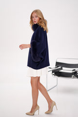 Woman wearing a navy blue poncho over a white dress with beige high heels on a white background