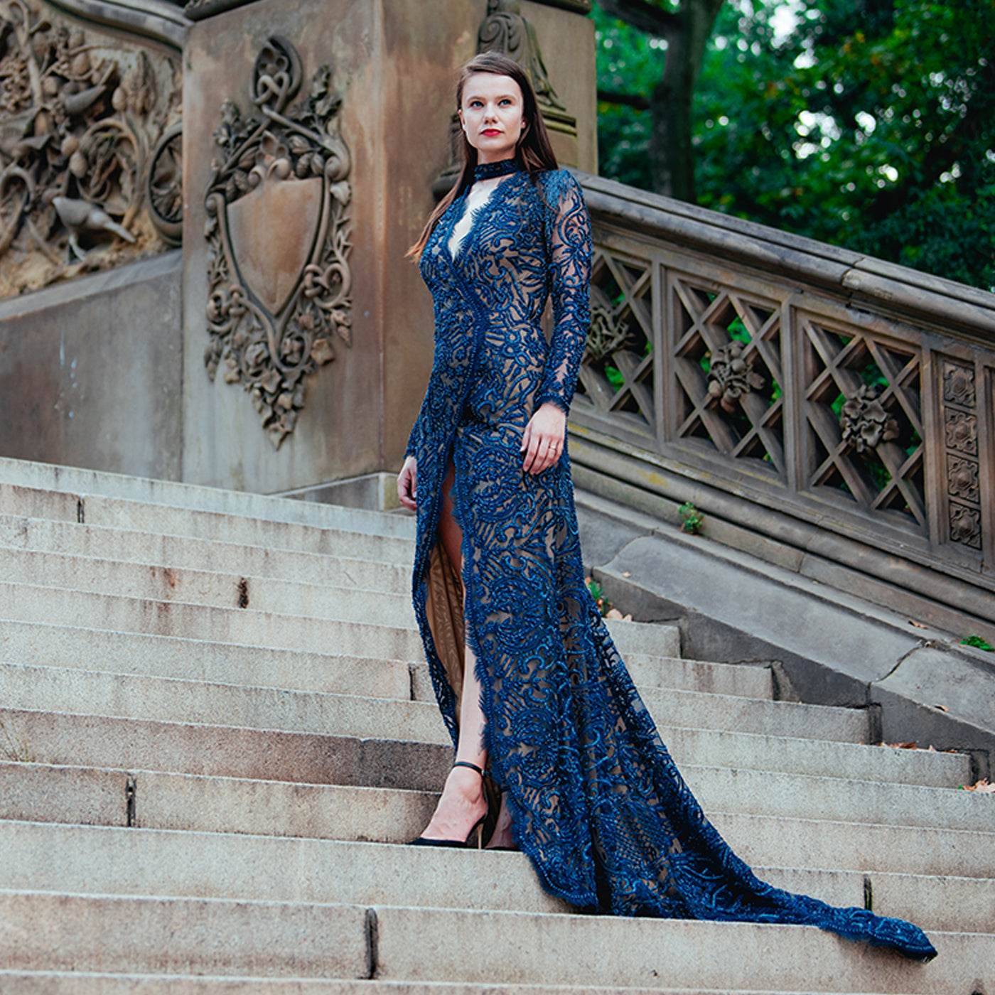 Woman in a blue lace dress standing on stone steps with decorative architecture.