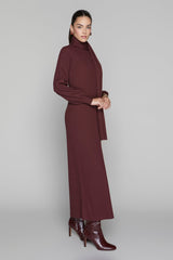 Woman wearing a long burgundy dress with a turtleneck on a gray background