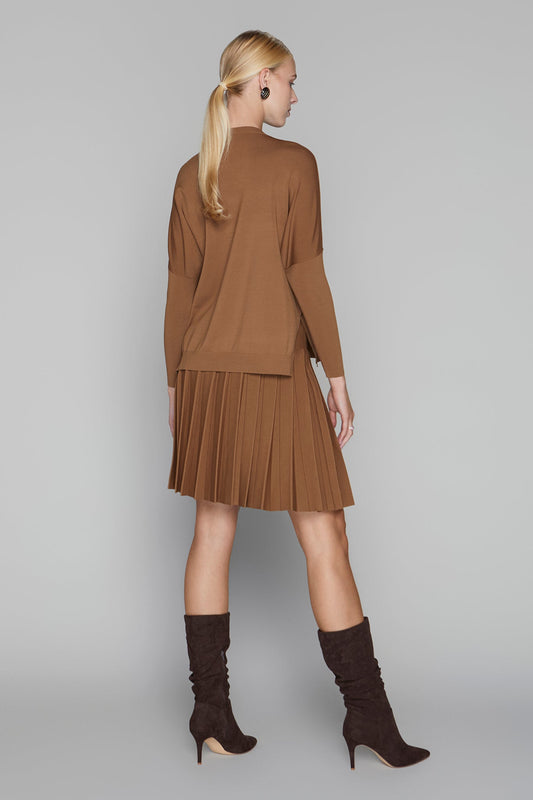 Woman wearing a brown outfit with a pleated skirt and high-heeled boots on a gray background