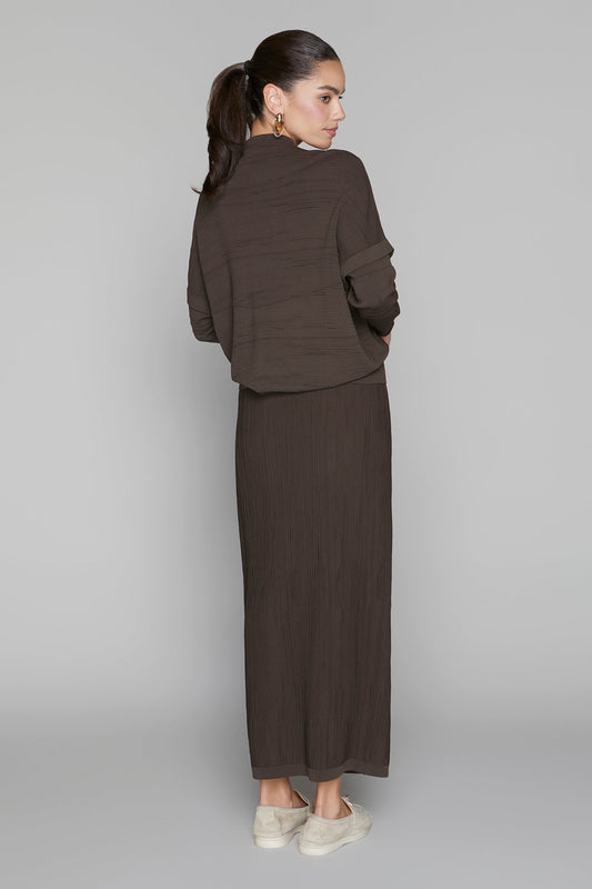 Woman wearing a brown outfit with a long skirt and jacket on a plain background