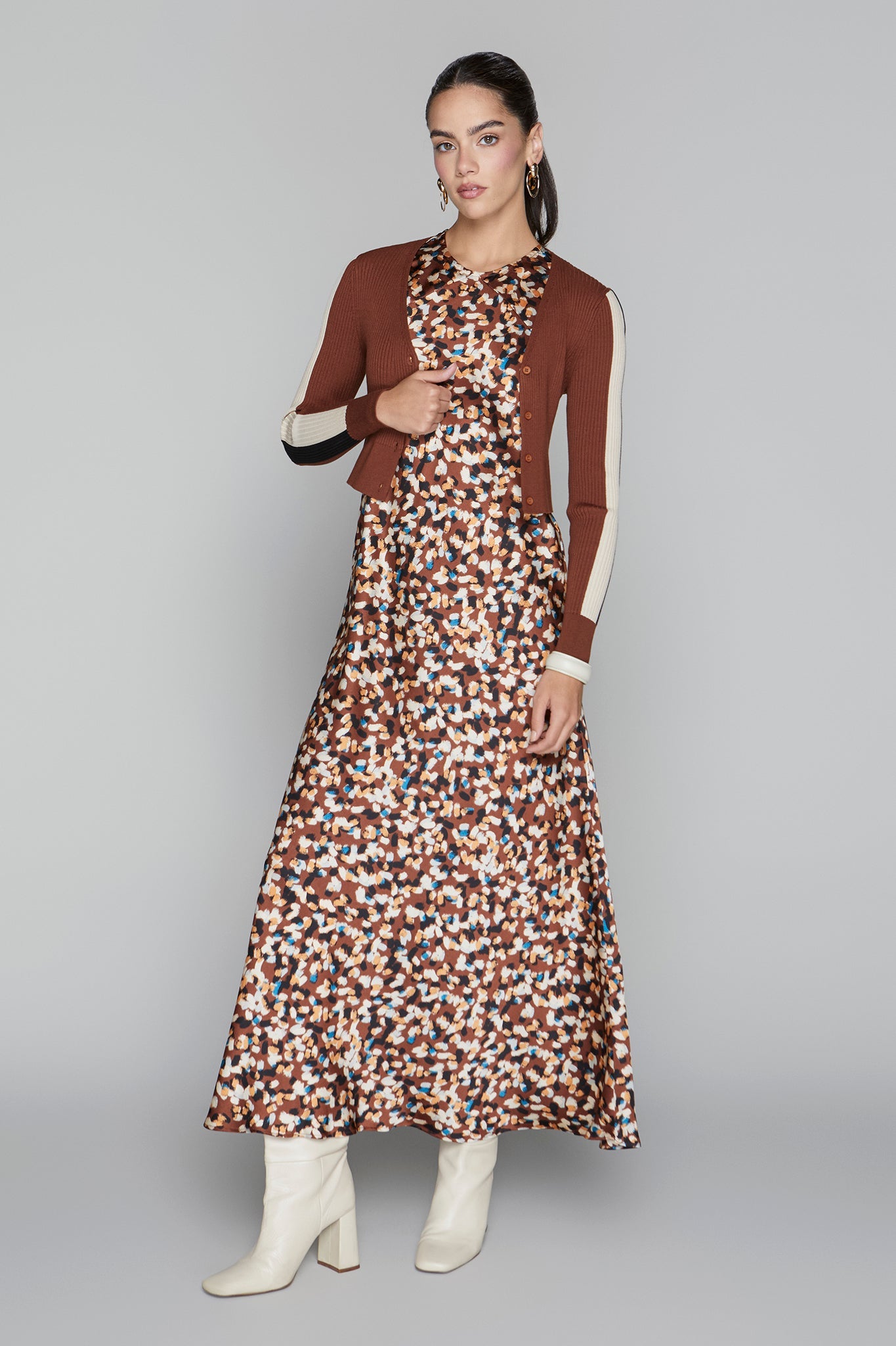 Woman wearing a patterned dress with a brown cardigan on a gray background