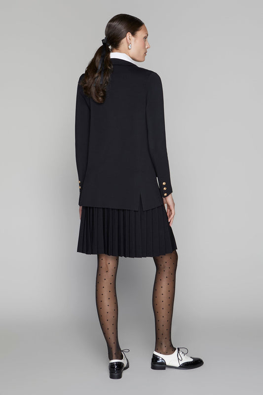 Woman wearing a black blazer and pleated skirt on a gray background