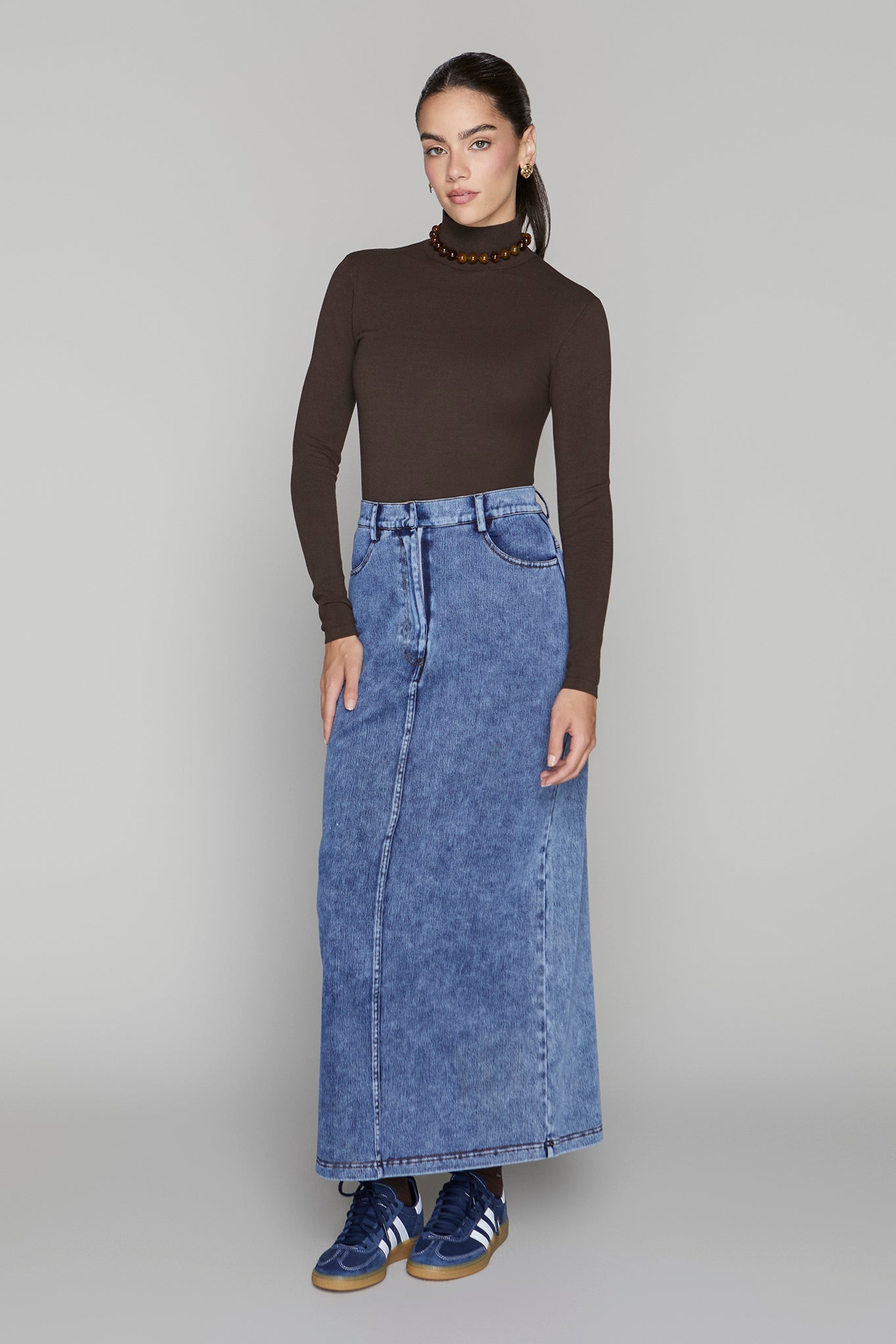Woman wearing a brown turtleneck and blue denim skirt on a gray background