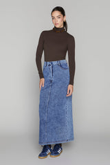 Woman wearing a brown turtleneck and blue denim skirt on a gray background