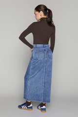 Woman wearing a brown long-sleeve top and blue denim skirt on a gray background