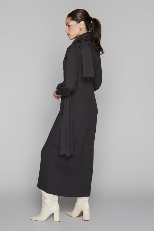 Woman wearing a long black coat on a gray background