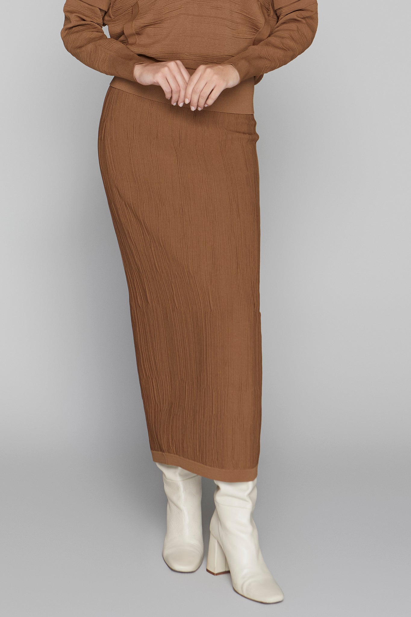 Person wearing a brown ribbed dress with white boots on a gray background