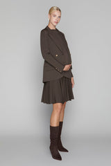Woman wearing a brown coat, skirt, and knee-high boots on a gray background
