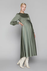 Woman wearing a green dress with long sleeves and white boots on a gray background