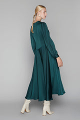 Woman wearing a green dress with long sleeves and a draped design, standing against a plain background.