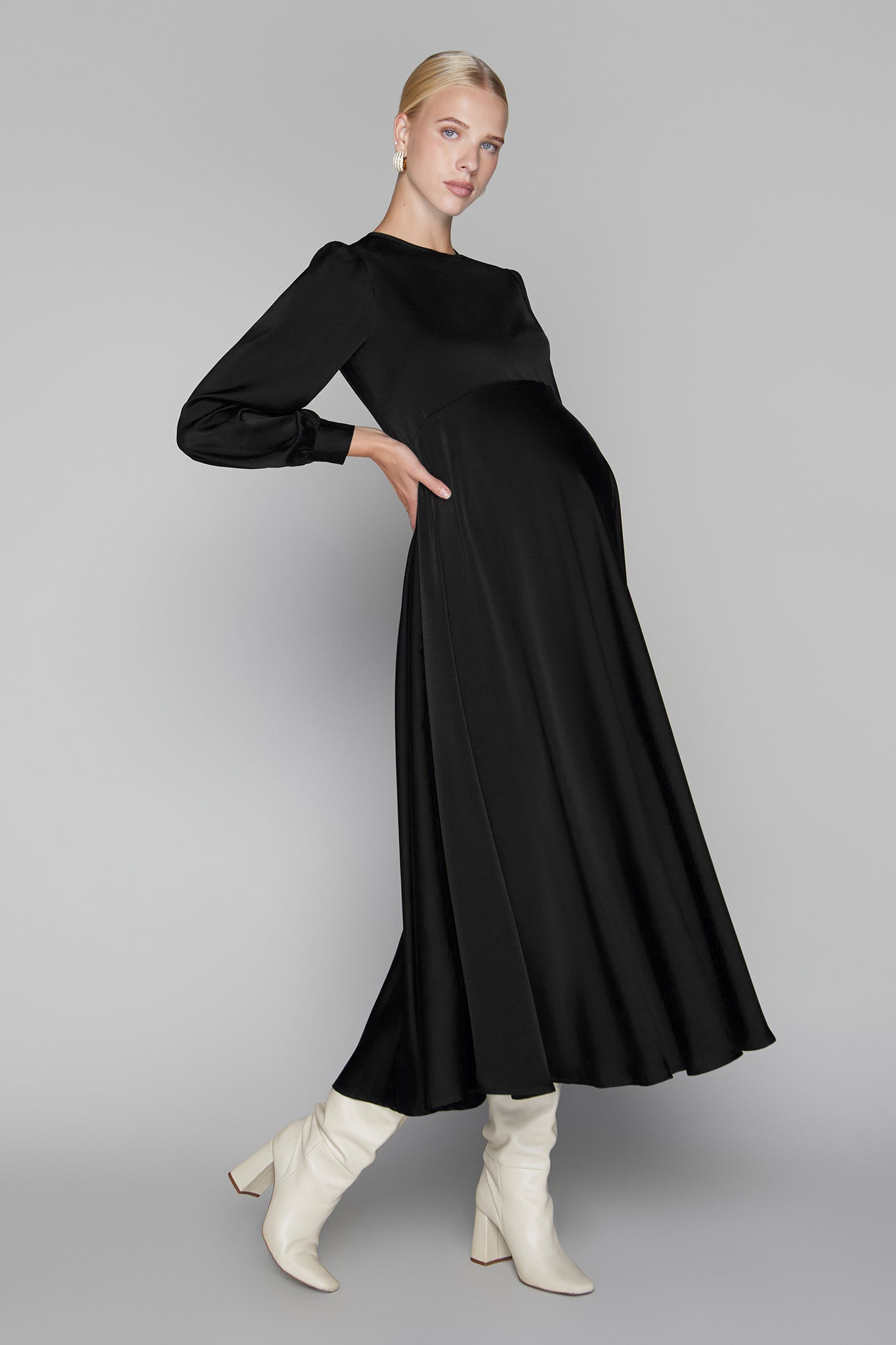 Woman wearing a black dress with long sleeves and white boots on a gray background