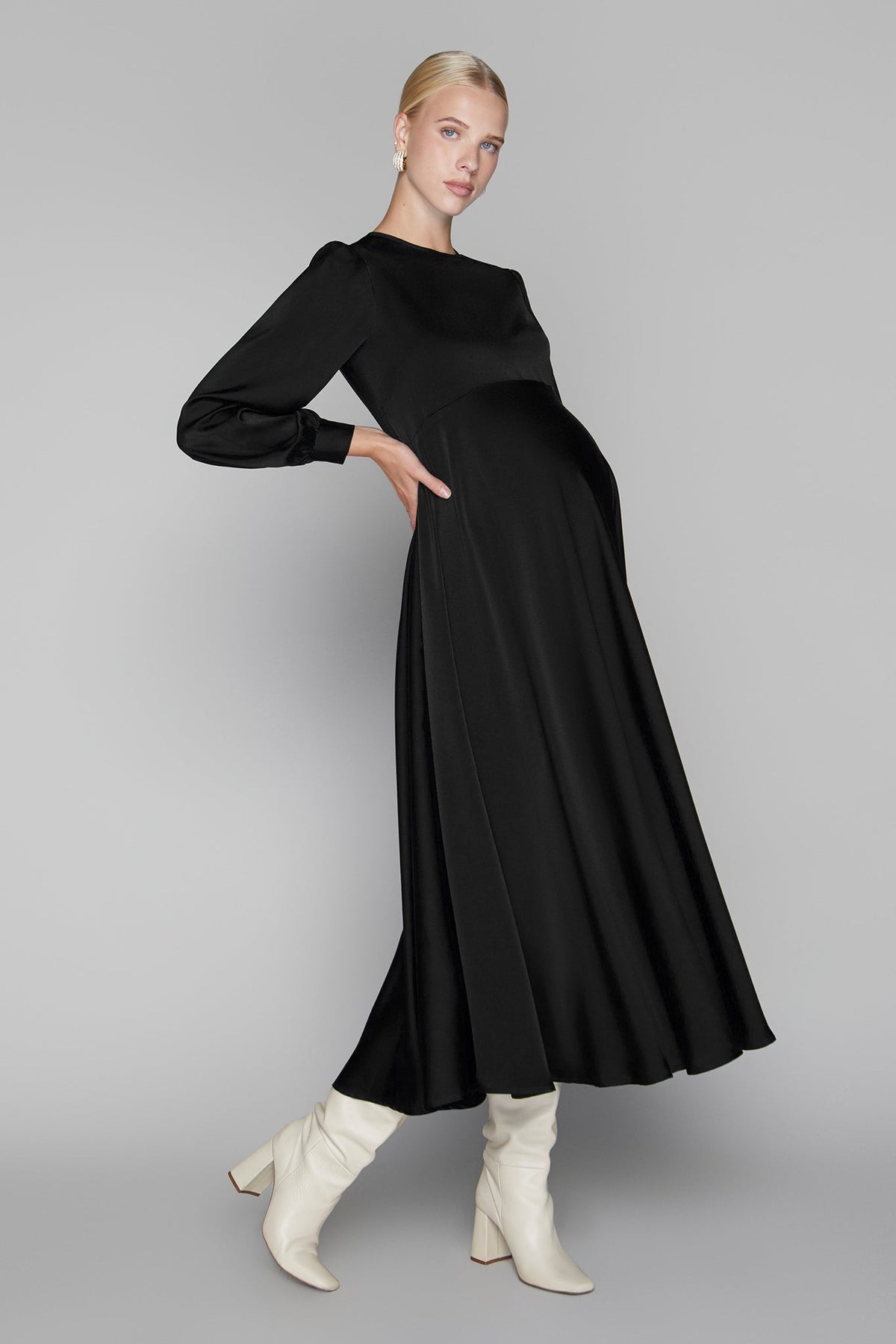 Woman wearing a black dress with long sleeves and white boots on a gray background