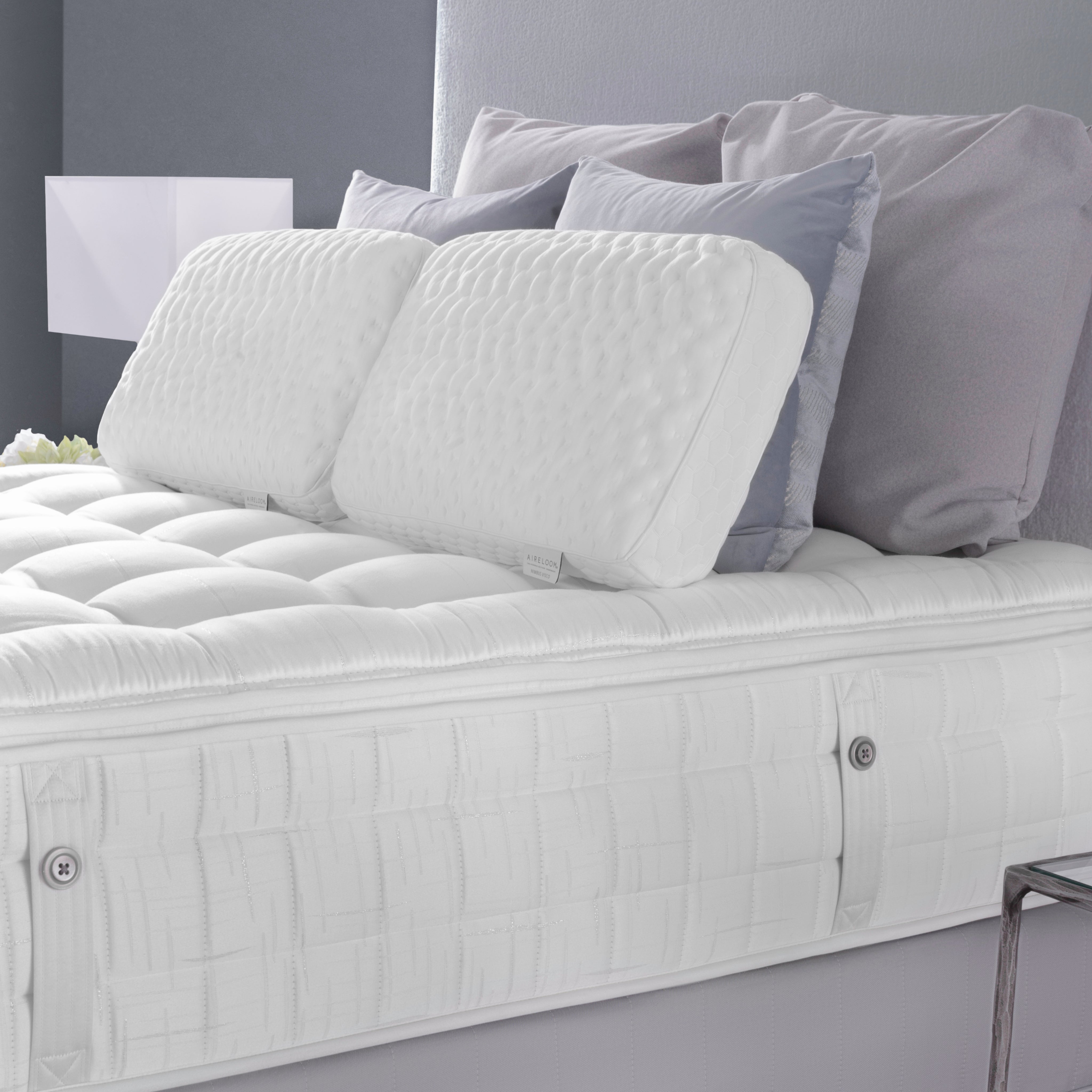 White mattress with decorative pillows on a bed against a gray wall.