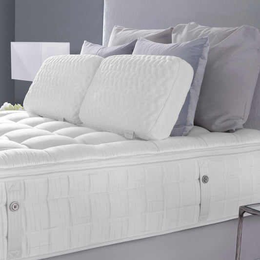 White mattress with decorative pillows on a bed against a gray wall.